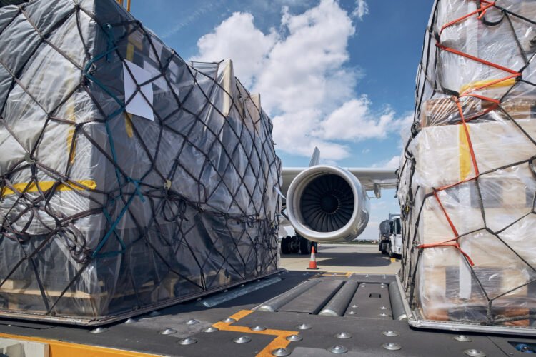 Preparation before flight. Loading of cargo containers against jet engine of freight airplane.
